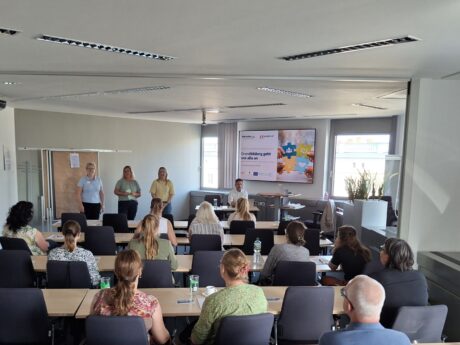 Blick in einen Konferenzraum. Vorn stehen drei Referenten.