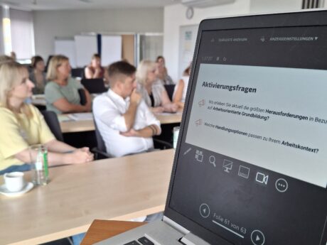 Blick vom Laptop, auf dem eine Präsentation zu sehen ist, ins Plenum.