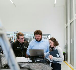 In einem Betrieb stehen drei Personen an einem Laptop.