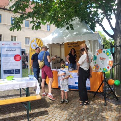 Es ist ein bunter Infostand des Projekts zu sehen, davor stehen mehrere Personen.