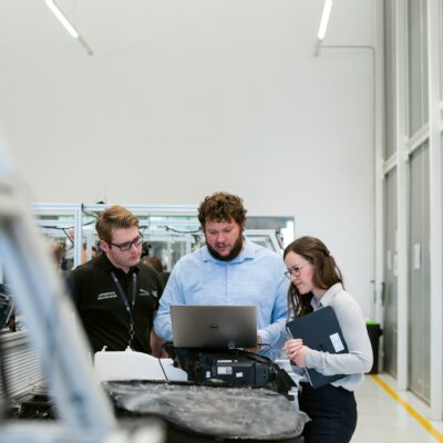 In einem Betrieb stehen drei Personen an einem Laptop.