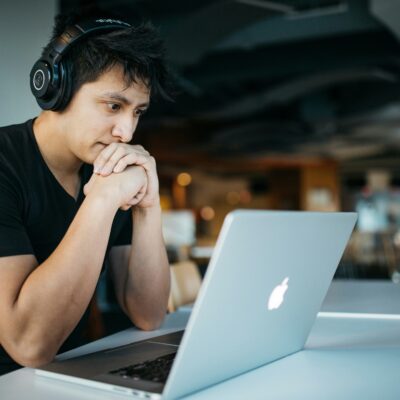 Ein Mann sitzt mit Kopfhörern vor einem Laptop. Er scheint einem Vortrag zu tauschen.
