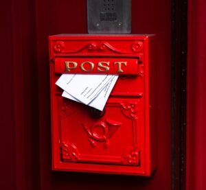 Ein roter Postkasten, Aus der Klappe ragen zwei Briefe hervor.