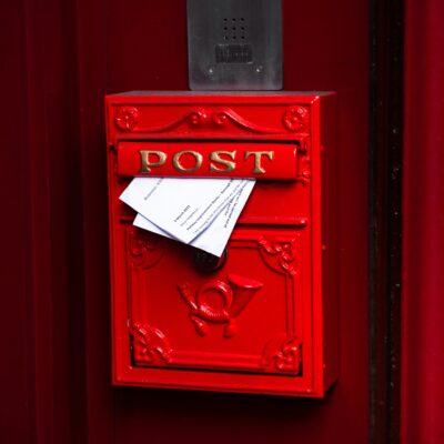 Ein roter Postkasten, Aus der Klappe ragen zwei Briefe hervor.