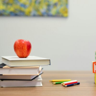 Links ist ein Bücherstapel gekrönt mit einem Apfel. In der Mitte liegen ein paar Stifte und rechts sind drei Bauklötze mit den Buchstaben A, B und C gestapelt.