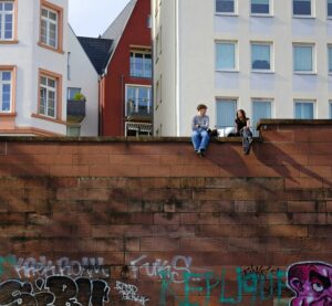 Ein Jung und ein Mädchen sitzen auf einer Mauer und unterhalten sich.
