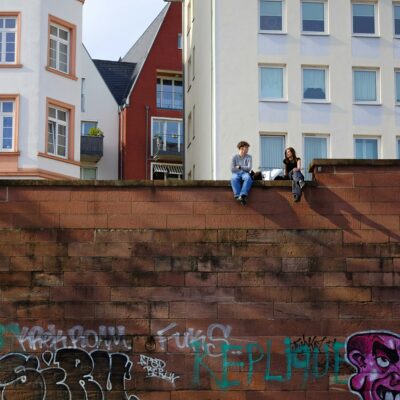 Ein Jung und ein Mädchen sitzen auf einer Mauer und unterhalten sich.