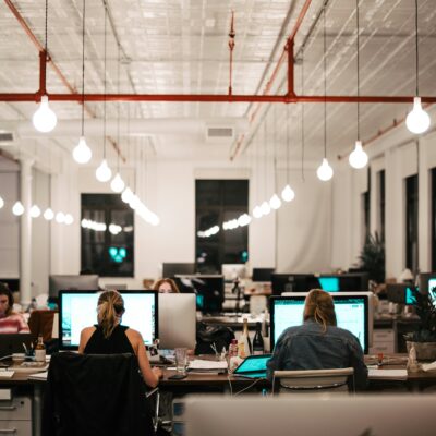 Blick in ein Großraumbüro. An den Bildschirmen sitzen verschiedene Personen und arbeiten.