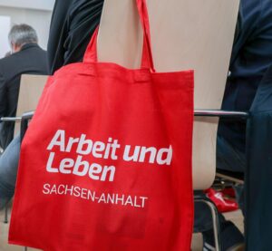 Blick in eine Veranstaltung von Arbeit und Leben Sachsen-Anhalt mit Fokus auf einen Beutel mit Logo.