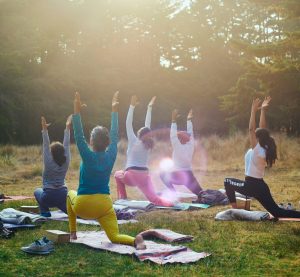 Fünf Frauen auf einer Wiese beim Yoga, die Sonne blendet.