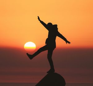 eine Person balanciert auf einem Stein vor dem Sonnenuntergang
