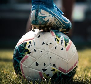 ein Fußball und darauf ein Fuß, der sich darauf abstützt