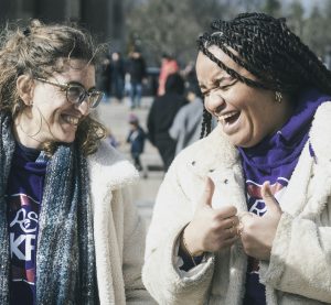 zwei weiblich gelesene Personen, die einander ansehen und lachen