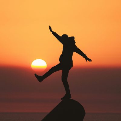 eine Person balanciert auf einem Stein vor dem Sonnenuntergang