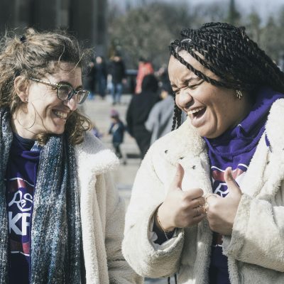 zwei weiblich gelesene Personen, die einander ansehen und lachen