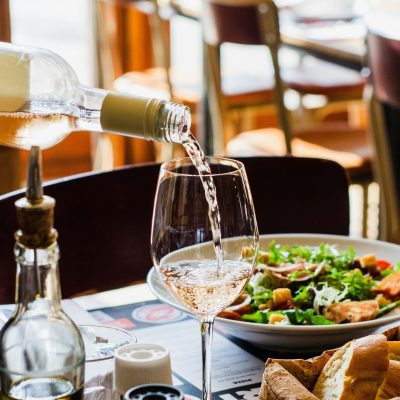 ein gedeckter Tisch, auf welchem ein Wein Glas mit Roséwein gefüllt wird