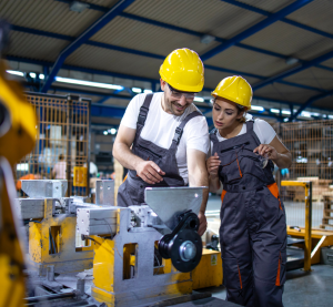 Blick in eine Fabrik. Ein Mann erklärt einer Frau auf einem Bildschirm die Bedienung der Maschine.