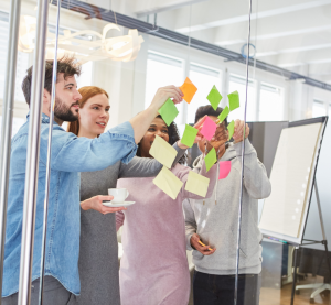 Eine Gruppe von Menschen steht vor einer Glaswand und platziert Klebezettel an der Wand.