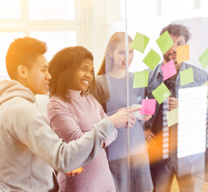 Vier Personen stehen an einer Glaswand und platzieren Klebezettel.