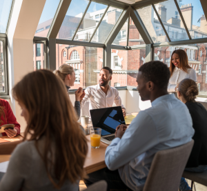Eine Gruppe von Menschen sitzt an einem Tisch mit Laptops und diskutiert.