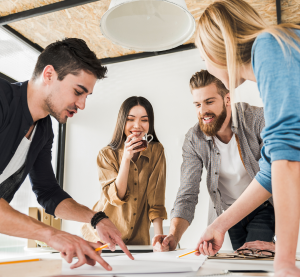 Zwei Männer und zwei Frauen lehnen über einen Tisch und zeigen auf die dort platzierten Papiere.