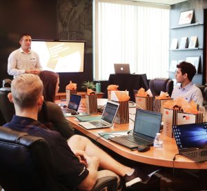 Gruppe sitzt mit Laptop an einem Konferenztisch und schaut nach vor zum Redner.