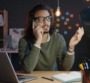 Mann mit Brille telefoniert im Dunkeln am Laptop