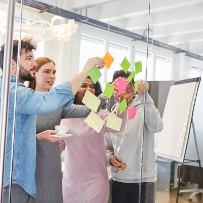 Eine Gruppe von Menschen steht vor einer Glaswand und platziert Klebezettel an der Wand.
