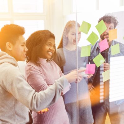 Vier Personen stehen an einer Glaswand und platzieren Klebezettel.