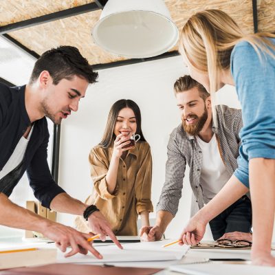 Zwei Männer und zwei Frauen lehnen über einen Tisch und zeigen auf die dort platzierten Papiere.