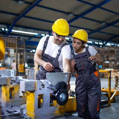 Blick in eine Fabrik. Ein Mann erklärt einer Frau auf einem Bildschirm die Bedienung der Maschine.