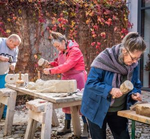 Drei Personen bearbeiten jeweils einen Steinblock mit Hammer und Meißel.