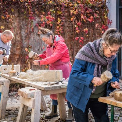 Drei Personen bearbeiten jeweils einen Steinblock mit Hammer und Meißel.