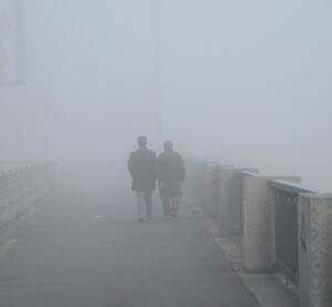Ein Pärchen geht auf einer Brücke. Um sie herum steigt der Nebel auf, sodass sie fast verschwinden.