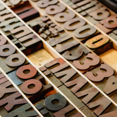 Zu sehen ist ein Setzkasten aus Holz, in dem verschiedene Buchstaben und Zahlen liegen.