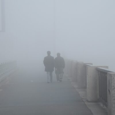 Ein Pärchen geht auf einer Brücke. Um sie herum steigt der Nebel auf, sodass sie fast verschwinden.