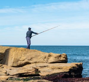 ein Angler steht mit ausgeworfener Angel am Meer