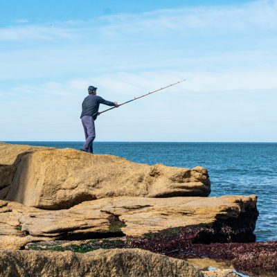 ein Angler steht mit ausgeworfener Angel am Meer