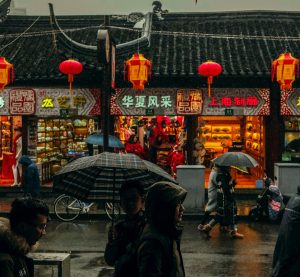 Blick auf einen chinesischen Straßenzug im Regen. Menschen laufen davor entlang
