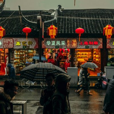 Blick auf einen chinesischen Straßenzug im Regen. Menschen laufen davor entlang