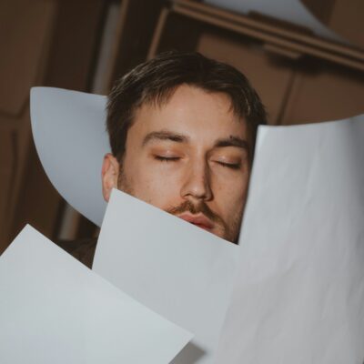 Person mit geschlossenen Augen hinter einem Stapel fallender Papiere