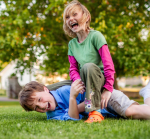 Zwei Kinder raufen sich auf einer Wiese. Sie lachen aber dabei noch.