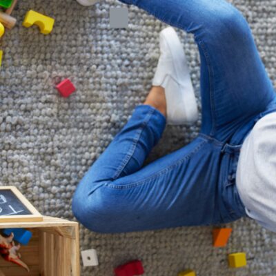Eine Frau sitzt auf dem Boden, auf dem mehrere Bausteine verteilt sind, hat die Hände an dem Kopf und schreit.