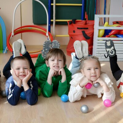 5 Kindergartenkinder liegen auf dem Bauch, haben den Kopf aufgestützt und schauen in die Kamera