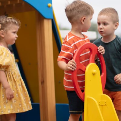 Zwei kleine Jungs streiten um das Steuer eines Spielplatzbootes. Eine kleines Mädchen Beobachtet sie.