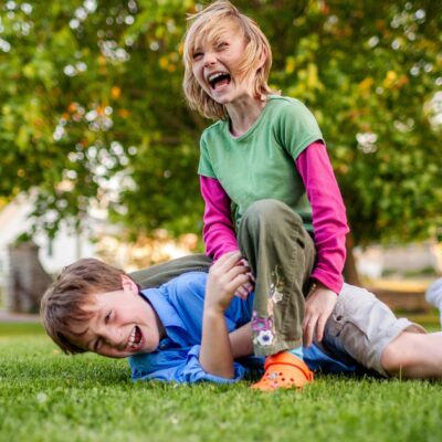 Zwei Kinder raufen sich auf einer Wiese. Sie lachen aber dabei noch.