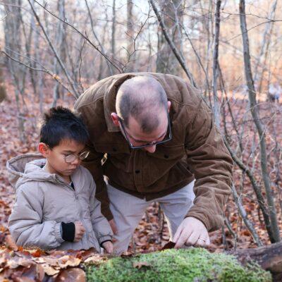Ein Mann und ein Junge stehen im Wald. Sie beugen sich über einen großen Stein und scheinen ein Tier zu beobachten.