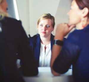 Bei einem Personalgespräch sitzt eine Mitarbeiterin im Mittelpunkt, während zwei weitere Personen aufmerksam zuhören und sich an dem Gespräch beteiligen.