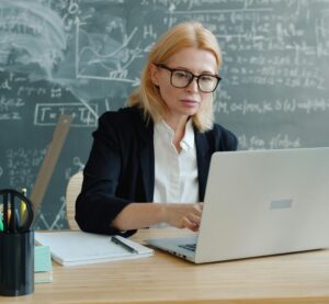 Eine Frau mit Brille sitzt an einem Laptop. Daneben liegen Stift und Notizblock.