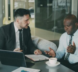 Zwei Geschäftsmänner diskutieren angespannt über Unterlagen an einem Tisch. Während einer seinen Standpunkt mit Gesten vertritt, wirkt der andere skeptisch – es deutet sich ein Konflikt über unterschiedliche Meinungen oder Entscheidungen an.